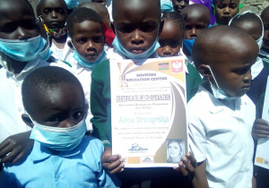 Zdjęcie przedstawia grupę kenińskich dzieci, jeden chłopców trzyma podziękowania dla nauczyciela za zaangażowanie w akcję.